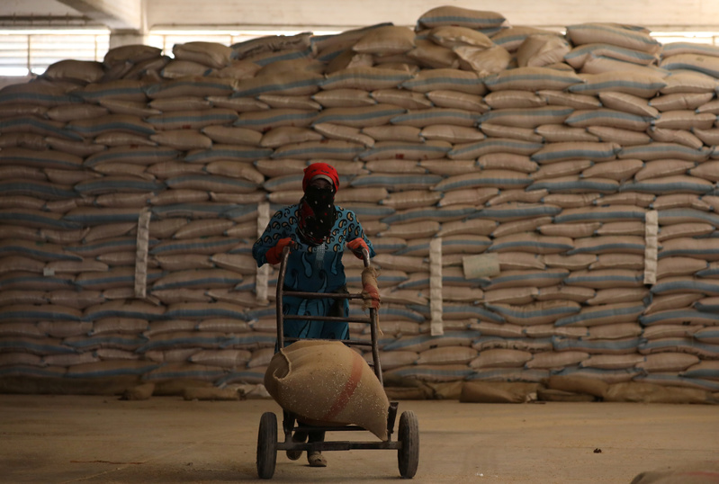 A woman pushes a cart loaded with a sack of wheat in Qamishli