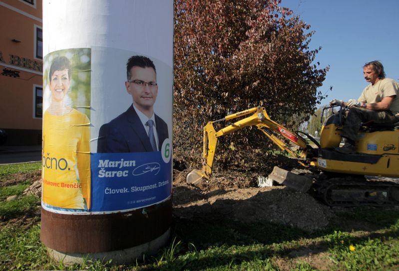 A worker uses an excavator next to the pole with presidential election campaign posters in Medvode