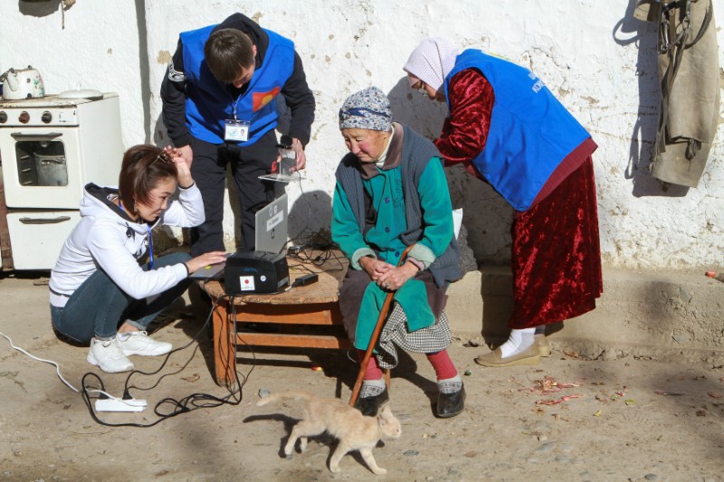 Visiting members of a local electoral commission conduct electronic identification of a voter during early voting at the presidential election in the village of Arashan outside Bishkek