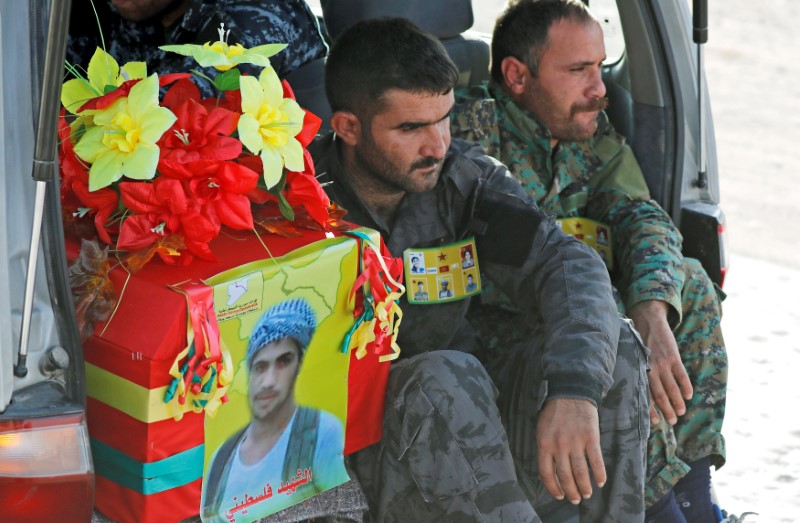 Fighters of Syrian Democratic Forces sit next to the coffin of their comrade killed by the Islamic State militants at the frontline in Deir al-Zour, during a funeral in Kobani