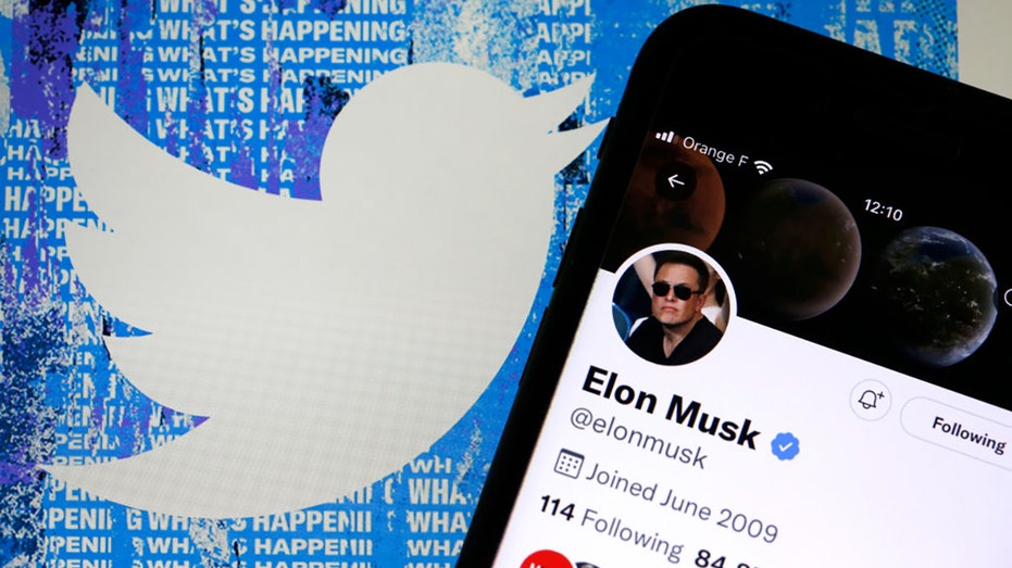 Elon Musk’s Twitter account is displayed on the screen of an iPhone in front of the homepage of the Twitter website