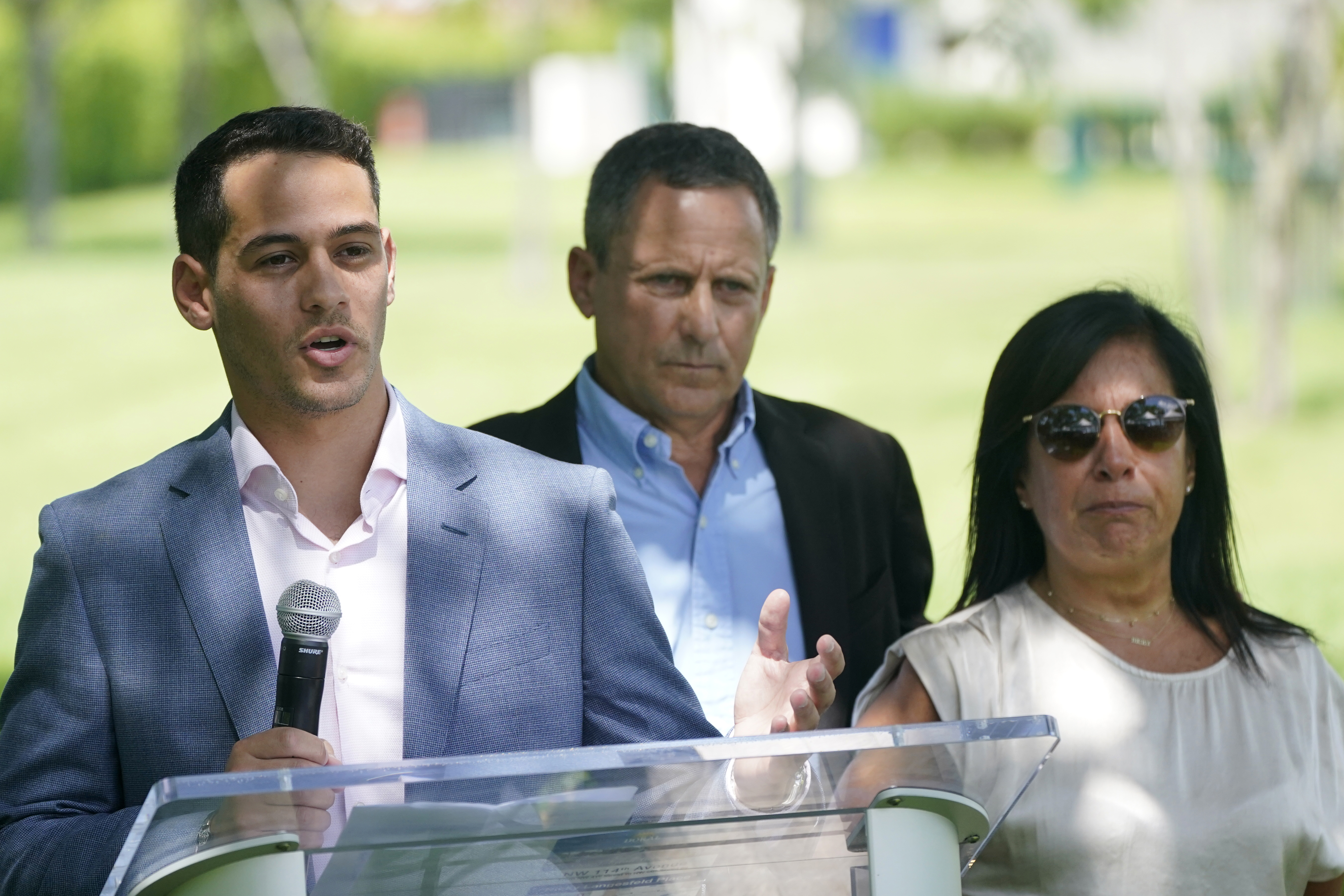 Martin Langesfeld, left, is joined by his parents Pablo and Andrea Langesfeld, as they speak at ceremony honoring Martin's sister and Pablo and Andrea's daughter Nicole "Nicky" Langesfeld, who died in the Surfside, Fla., condo collapse, before unveiling a sign for "Nicky Langesfeld Place," Wednesday, June 22, 2022, in Doral, Fla. Langesfeld grew up in Doral before moving to Surfside. (AP Photo/Wilfredo Lee)