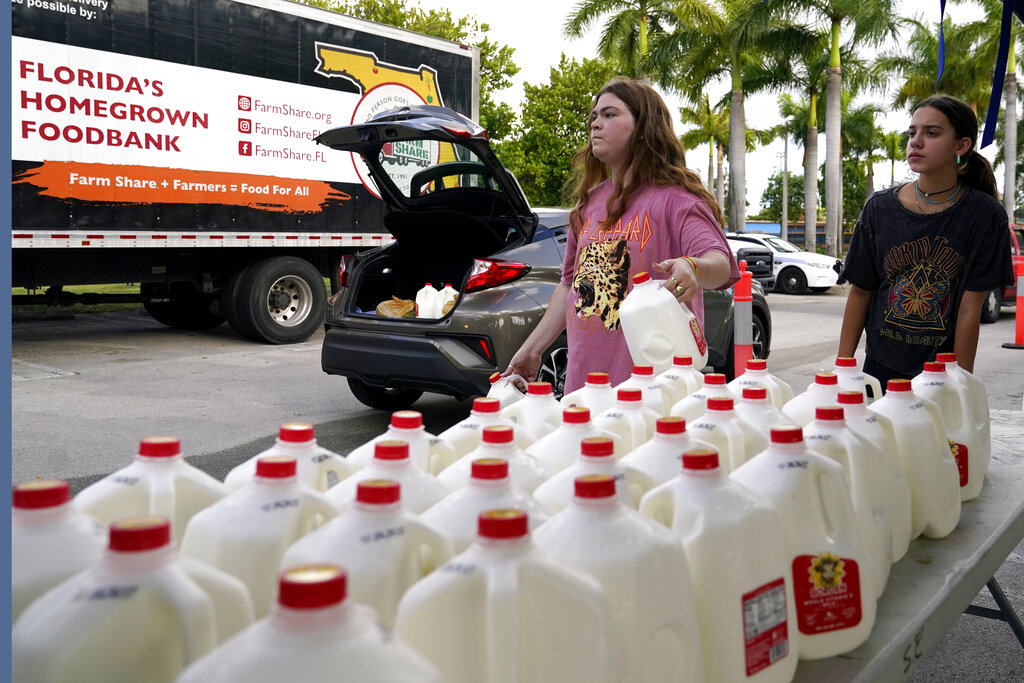 Vanessa Correa, left, and Gigi Fiske, right, pass out gallons of milk at a food distribution held by the Farm Share food bank, Wednesday, July 20, 2022, in Miami. Long lines are back at food banks around the U.S. as working Americans overwhelmed by inflation turn to handouts to help feed their families. (AP Photo/Lynne Sladky)