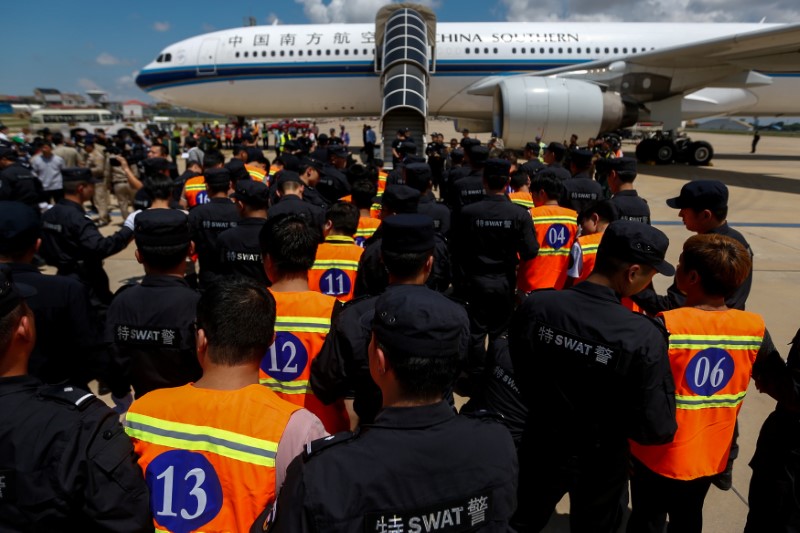 Chinese nationals (in orange vests) who were arrested over a suspected internet scam, are escorted by Chinese police officers before they were deported at Phnom Penh International Airport, in Phnom Penh