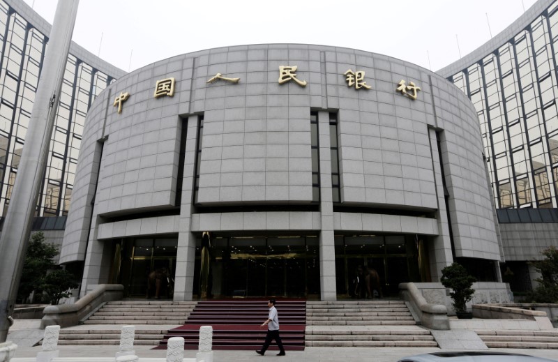 FILE PHOTO: A staff member walks in front of the headquarters of the People's Bank of China, the central bank, in Beijing