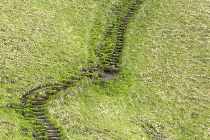 A staircase cut into the grass rises up a hillside in Skogarfoss, Iceland