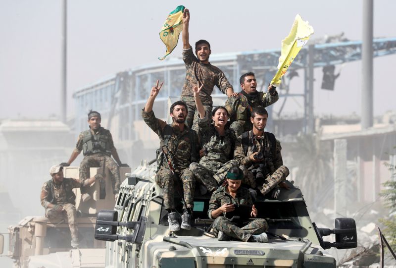 SDF fighters ride atop military vehicles as they celebrate victory in Raqqa