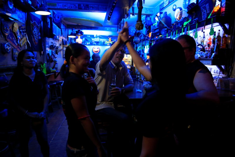 American James John Goodman, 51, does a high-five with female servers inside a bar in Subic, north of Manila