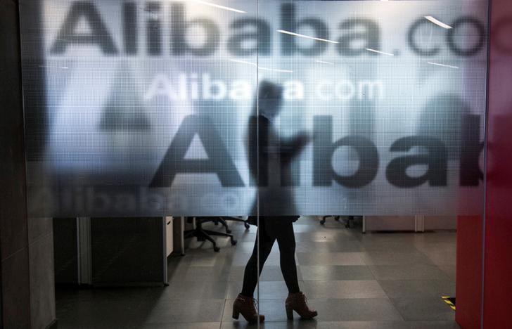 FILE PHOTO: An employee is seen behind a glass wall with the logo of Alibaba at the company's headquarters on the outskirts of Hangzhou, Zhejiang province