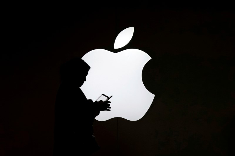 A woman looks at the screen of her mobile phone in front of an Apple logo outside its store in Shanghai