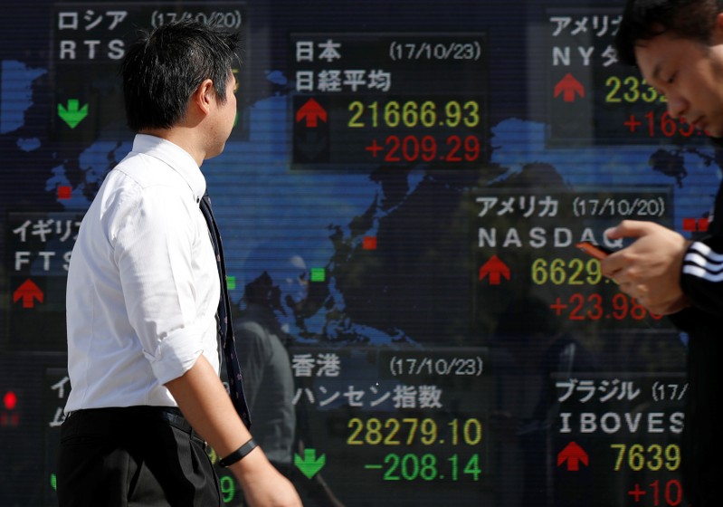Passersby walk past an electronic board showing market indices outside a brokerage in Tokyo