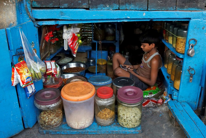 A boy uses a mobile phone as he sits inside his father's snacks shop along a road in Kolkata