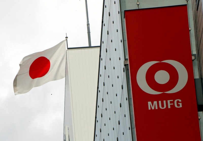 FILE PHOTO: Japan's national flag is seen behind the logo of Mitsubishi UFJ Financial Group Inc (MUFG) at its bank branch in Tokyo