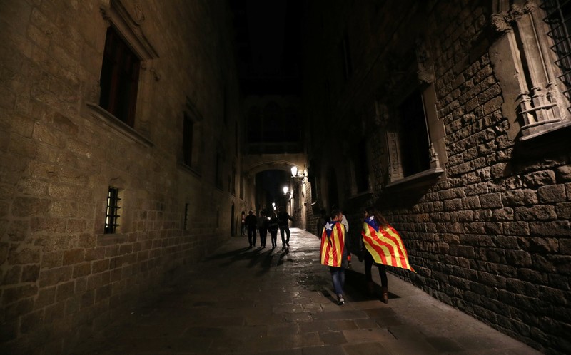 A couple wearing Esteladas (Catalan Separatist flag) as capes walk by the street as they leave a protest in support of the members of the dismissed Catalan cabinet, in Barcelona