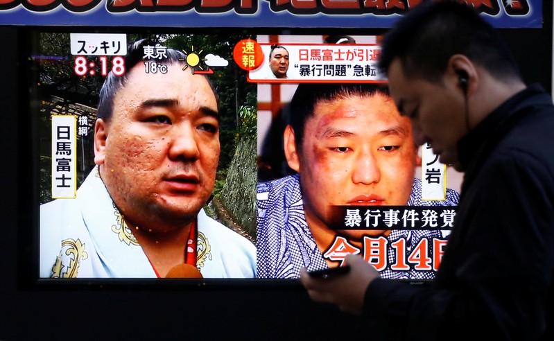 People walk past a street monitor showing Sumo grand champion Harumafuji (L) and junior wrestler Takanoiwa in Tokyo