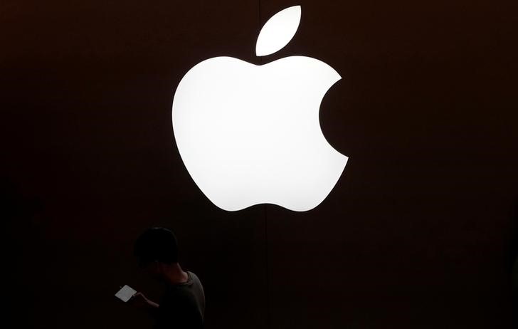 FILE PHOTO - A man looks at the screen of his mobile phone in front of an Apple logo outside its store in Shanghai