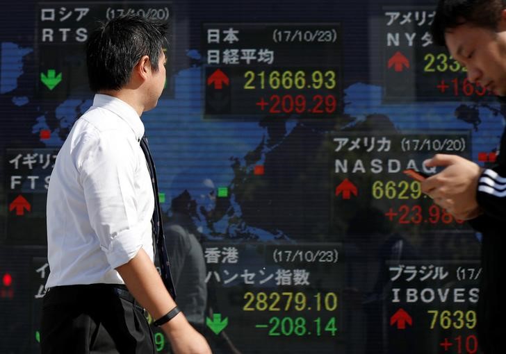 Passersby walk past an electronic board showing market indices outside a brokerage in Tokyo