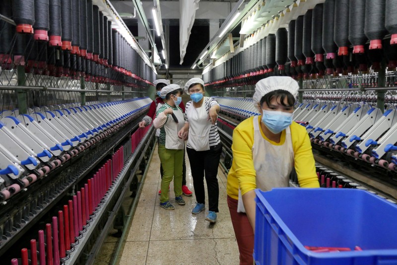 FILE PHOTO: A worker jokes and beckons at her colleague as she rolls away carts of unused tools between rows of spinning machine at a factory owned by Hong Kong's Novetex Textiles Limited in Zhuhai City, Guangdong Province, China