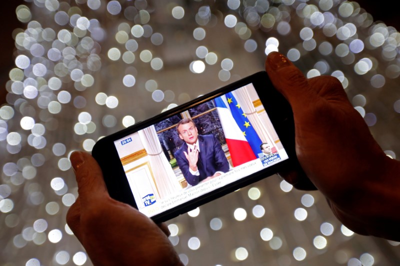 French President Emmanuel Macron is seen on the screen of an iPhone in Marseille as he gives the traditional New Year speech during a prime time news broadcast at the Elysee Palace in Paris