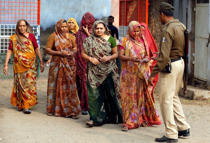 A policeman checks identity papers of women as they arrive to cast their votes at a polling station during the first phase of Gujarat state assembly election in Panshina village of Surendranagar district