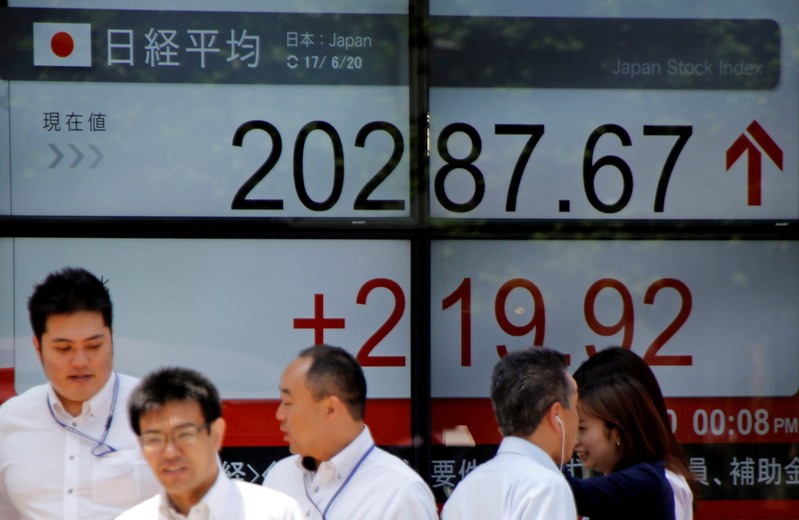 FILE PHOTO: People walk past an electronic board showing Japan's Nikkei average outside a brokerage in Tokyo