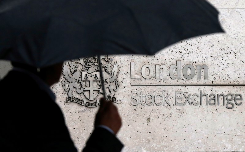 FILE PHOTO:A man shelters under an umbrella as he walks past the London Stock Exchange