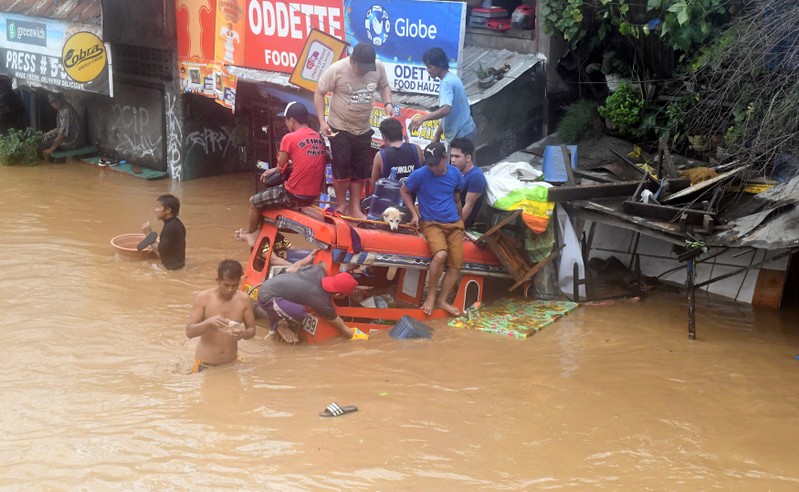 Residents are seen on the top of a partially submerged vehicle along a flooded road in Cagayan de Oro city in the Philippines