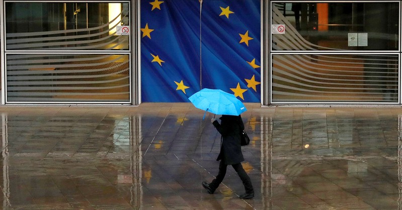 A woman holds an umbrella as she walks past the flag of the European Union outside the European Commission in Brussels, Belgium.