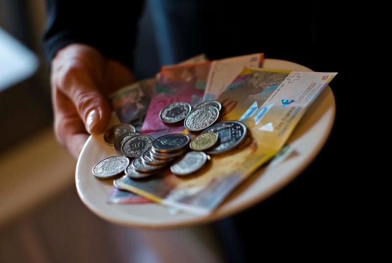 A waitress presents a plate with various Swiss Franc coins and notes in this picture illustration in a restaurant in Zurich