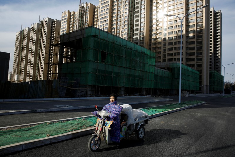 A man rides an electric tricycle past residential apartment blocks under construction on the outskirts of Beijing