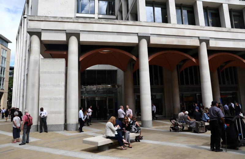 People stand and sit outside the London Stock Exchange in Paternoster Square, London