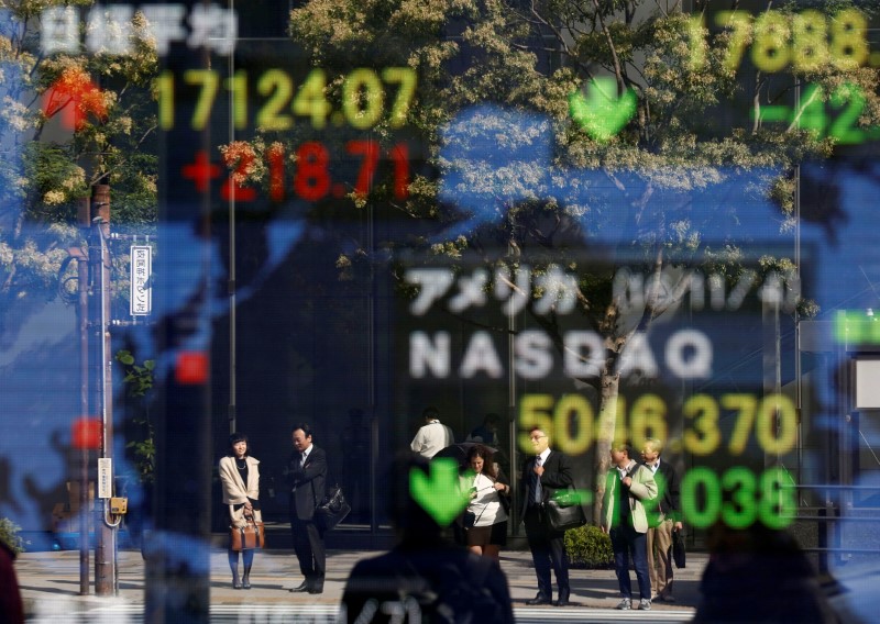 People are reflected in a display showing the Nikkei average and the NASDAQ average of the U.S outside a brokerage in Tokyo