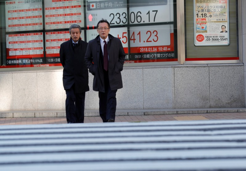 Pedestrians walk past an electronic board displaying the Nikkei average outside a brokerage in Tokyo