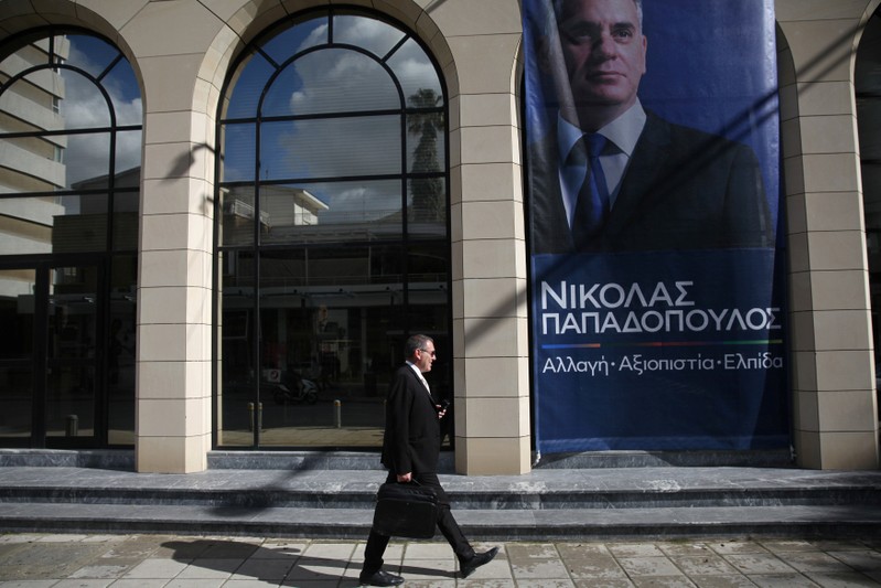 A man walks in front of a pre-election poster of Presidential candidate Nikolas Papadopoulos leader of the center-right DIKO party in Nicosia