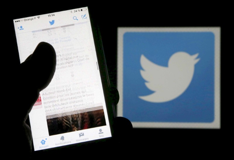 FILE PHOTO: A man reads tweets on his phone in front of a displayed Twitter logo in Bordeaux, southwestern France