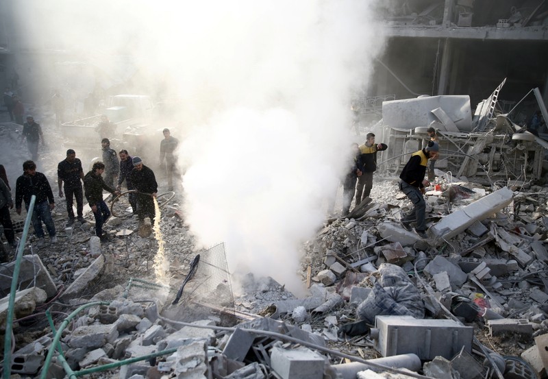 People stand on rubble of damaged buildings after airstrike in Hamoria, Damascus