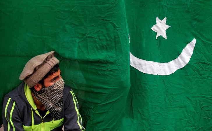 A masked protester sits next to a flag of Pakistan during an anti-Indian protest in Srinagar