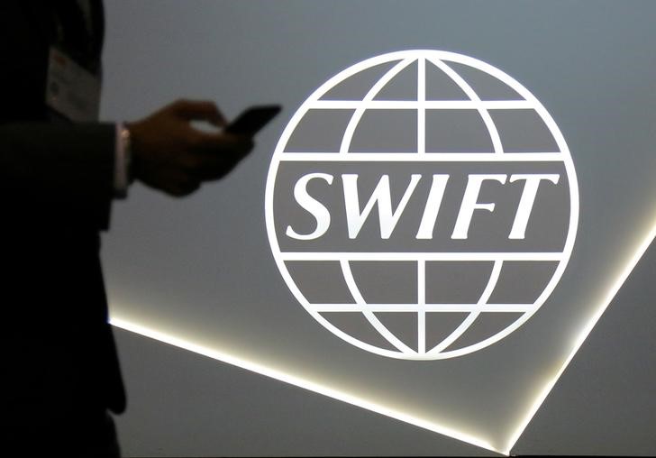 FILE PHOTO:A man using a mobile phone passes the logo of global secure financial messaging services cooperative SWIFT at the SIBOS banking and financial conference in Toronto
