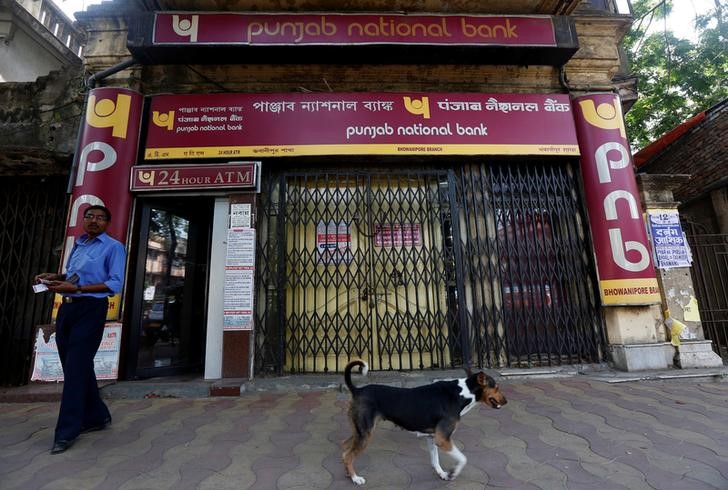 A man exits Punjab National Bank's building as a stray dog walks past in Kolkata