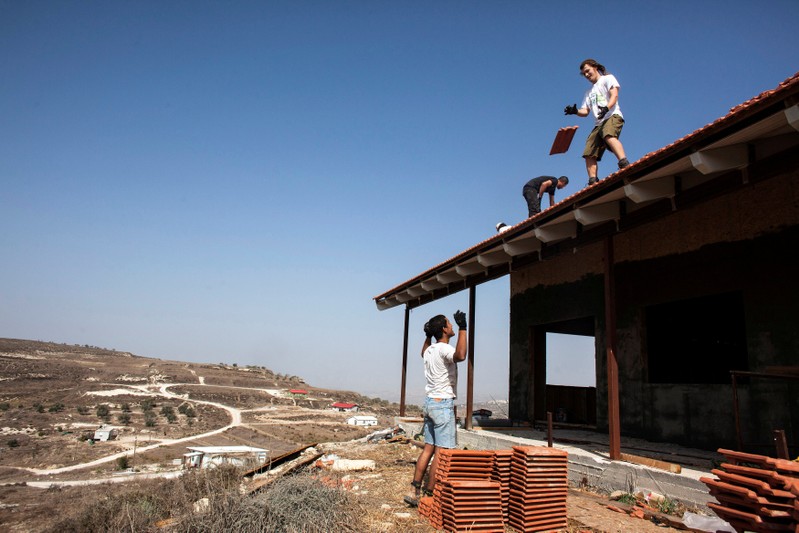 FILE PHOTO: Men work on the roof of a house under construction in the unauthorised Jewish settler outpost of Havat Gilad, south of the West Bank city of Nablus