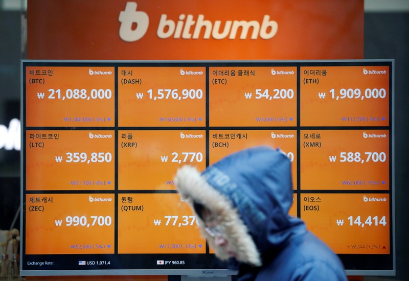 FILE PHOTO: A man walks past an electric board showing exchange rates of various cryptocurrencies at Bithumb cryptocurrencies exchange in Seoul