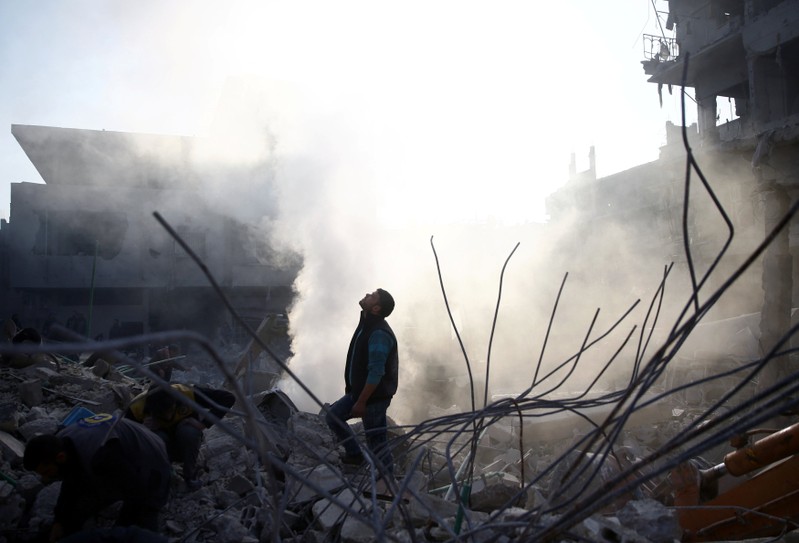 Man stands on rubble of damaged buildings after airstrike in Hamoria, Damascus