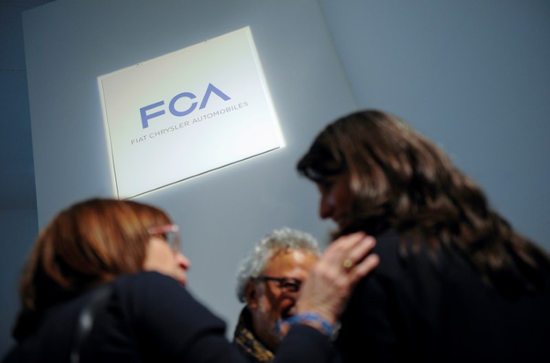 FILE PHOTO: People talk as they stand next to a logo of Fiat Chrysler Automobiles (FCA) in Turin
