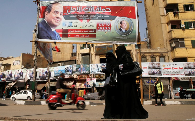 Woman wearing a full veil (niqab) walk in front of posters of Egypt's President Abdel Fattah al-Sisi during the preparations for tomorrow's presidential election in Cairo