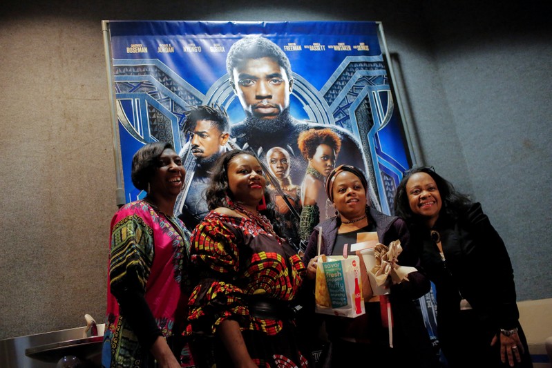 A group of women pose for a photo in front of a poster advertising the film 