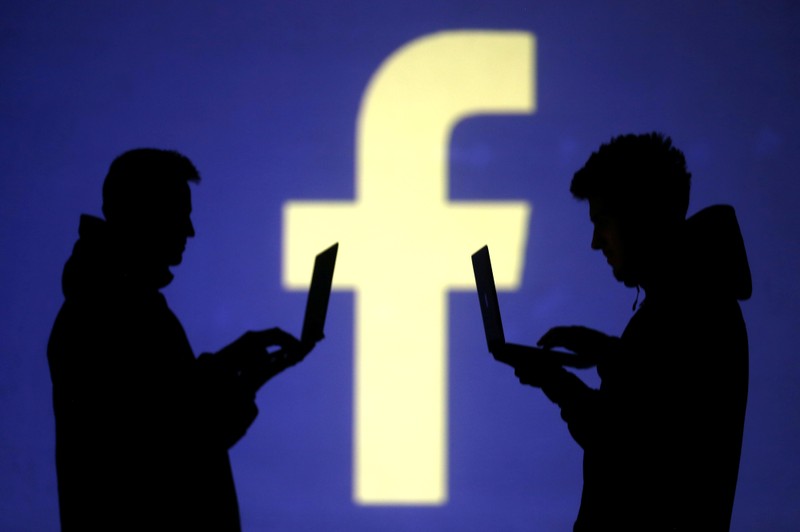 Silhouettes of laptop users are seen next to a screen projection of Facebook logo in this picture illustration