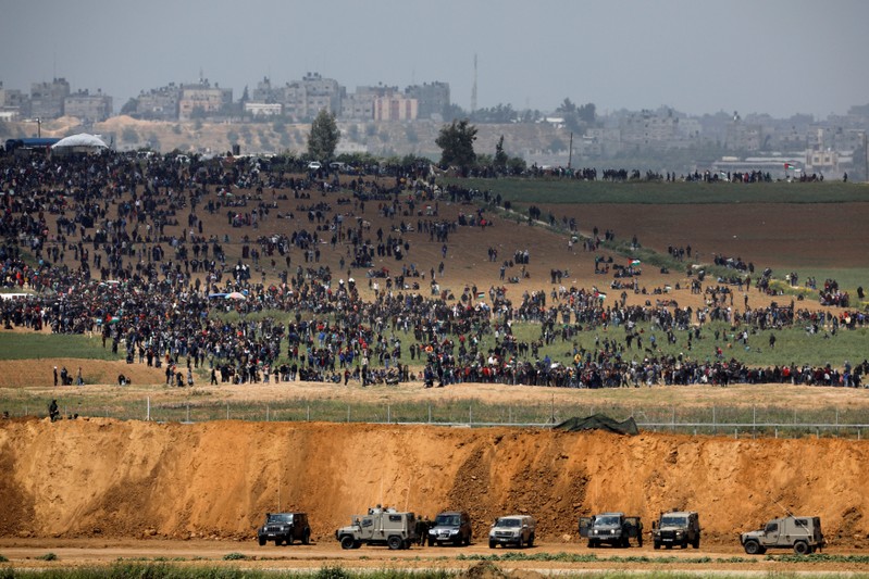 Israeli military vehicles are seen next to the border on the Israeli side of the Israel-Gaza border, as Palestinians demonstrate on the Gaza side of the border