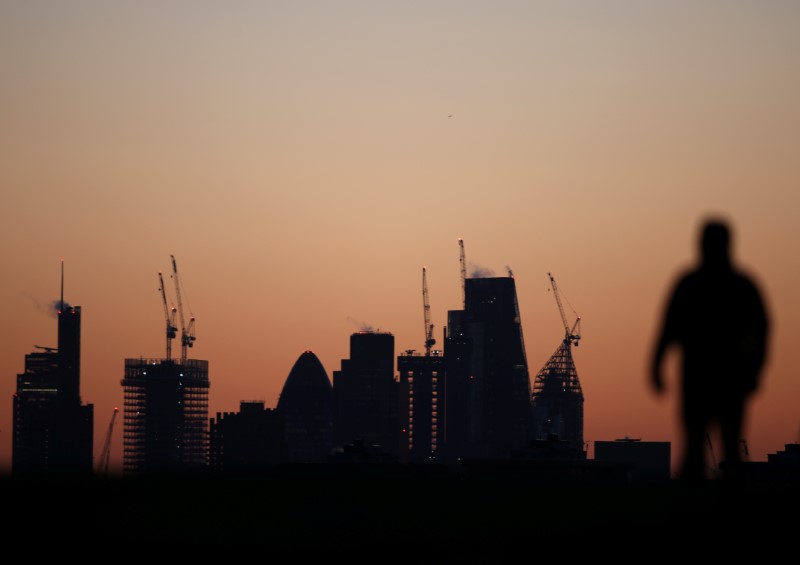 A man walks accross Primrose Hill as dawn breaks behind construction cranes in the City of London