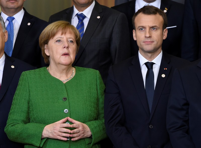 France's President Emmanuel Macron speaks with German Chancellor Angela Merkel as they gather for a family photo during a High Level Conference on the Sahel at the European Commission in Brussels