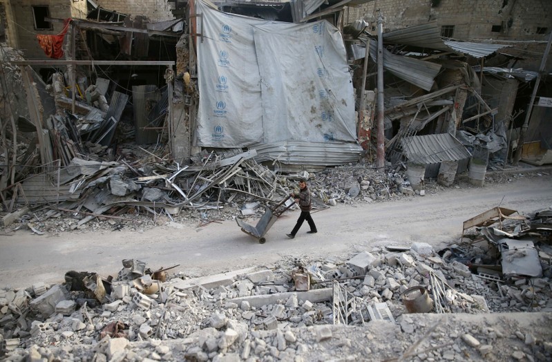 A man pushes a cart past damaged buildings at the besieged town of Douma